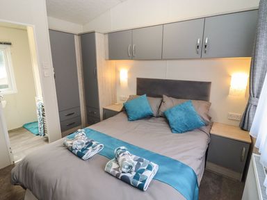 A bedroom with a double bed towels on bed gray and blue bedding built in wardrobes bedside cabinets and wall lights at Blossom Vale Lodge in Evesham