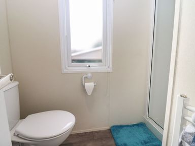 A small bathroom with a toilet blue bath mat and a window at Blossom Vale Lodge in Evesham