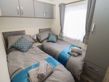 A bedroom with two single beds gray bedding and blue runners with towels on each bed at Blossom Vale Lodge in Evesham