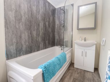 A bathroom with a bathtub a blue towel a sink with storage and a mirror at Blossom Vale Lodge in Evesham