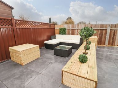 A fenced outdoor patio with a corner sofa a glass coffee table wooden benches and small potted plants at Blossom Vale Lodge in Evesham