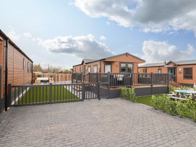 An exterior view of a wooden lodge with a fenced patio and artificial grass at Blossom Vale Lodge in Evesham