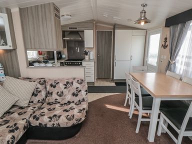 A combined kitchen and dining area with a floral patterned sofa a wooden dining table with chairs and kitchen appliances at Rose Bank D8 in Primrose Valley