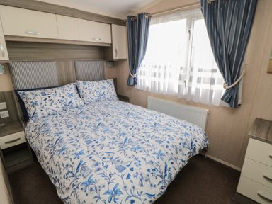 A bedroom with a double bed with blue and white floral bedding and blue curtains at Rose Bank D8 in Primrose Valley
