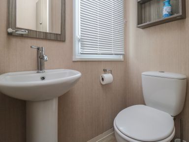 A bathroom with a pedestal sink toilet window with blinds and a wall-mounted shelf with an air freshener at Rose Bank D8 in Primrose Valley