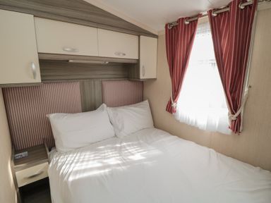 A bedroom with a double bed pillows cabinets and a window with red curtains at Rose Bank D8 in Primrose Valley