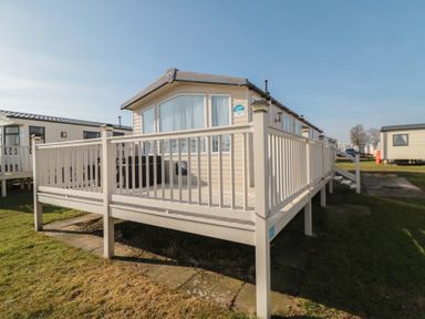 A mobile home with a raised deck and railing on grass at Rose Bank D8 in Primrose Valley