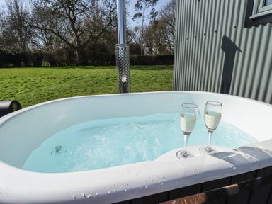 An outdoor hot tub with two glasses of champagne and a grassy field in the background at Buttercup in Ashby-cum-Fenby near Waltham