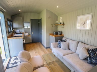 A small living area with two chairs a sofa with pillows a glass coffee table and a kitchenette at Buttercup Ashby-cum-Fenby near Waltham