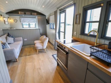 A kitchen with a sink oven and stovetop next to a living area with a sofa two chairs and a glass coffee table at Buttercup in Ashby-cum-Fenby near Waltham
