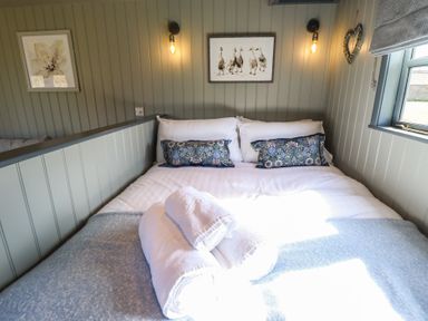 A bed with white linens and blue patterned pillows in a small room with gray paneled walls at Buttercup in Ashby-cum-Fenby near Waltham