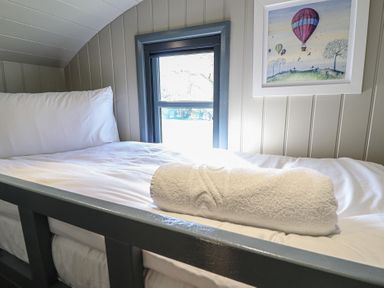 A single bed with a rolled towel on top under a small window with a framed picture on the wall at Buttercup in Ashby-cum-Fenby near Waltham