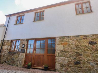 A building exterior with stone lower walls and white upper walls with wooden windows and doors at The Baler House in Hayle