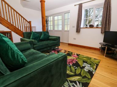 A living room with green sofas floral rug wooden staircase and a television at The Baler House in Hayle