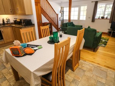 A dining table with wooden chairs in a room with a kitchen and living area at The Baler House in Hayle