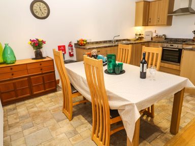 A kitchen with wooden cabinets a dining table with chairs and a sideboard with vases and flowers at The Baler House in Hayle