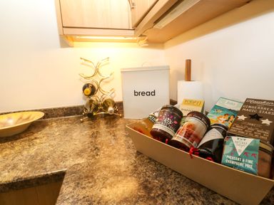 A kitchen counter with a bread box paper towel holder wine rack and a gift basket with jars and boxes at The Baler House in Hayle