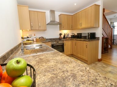 A kitchen with wooden cabinets a stainless steel sink an oven and a fruit basket on the counter at The Baler House in Hayle