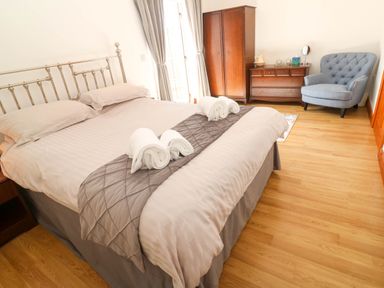 A bedroom with a bed with rolled towels a wardrobe a chest of drawers and a blue armchair at The Baler House in Hayle