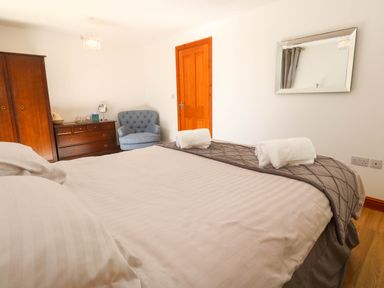 A bedroom with a double bed white pillows wooden wardrobe wooden dresser blue armchair and a wall mirror at The Baler House in Hayle