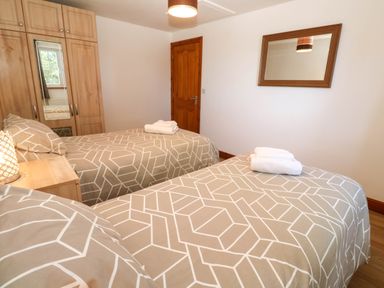 A bedroom with two single beds a wooden wardrobe a wall mirror and a wooden door at The Baler House in Hayle