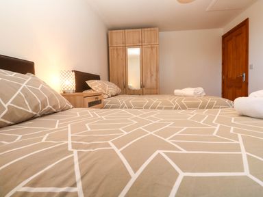 A bedroom with two single beds bedside table lamp wooden wardrobe and wooden door at The Baler House in Hayle