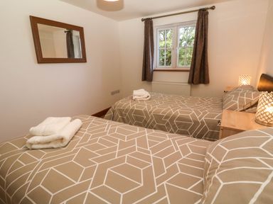 A bedroom with two single beds covered with patterned bedding a window with curtains and a wall mirror at The Baler House in Hayle