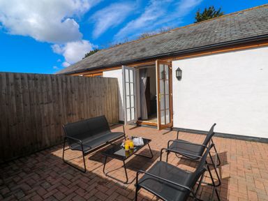 An outdoor patio area with black metal chairs and a table with drinks and a magazine at The Baler House in Hayle