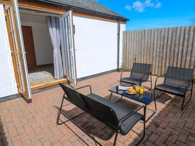 An outdoor patio with black metal chairs and a table with croissants and orange juice at The Baler House in Hayle