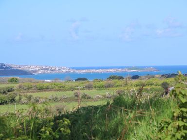 A coastal landscape with green fields and shrubs in the foreground and a town by the sea in the background at The Baler House in Hayle