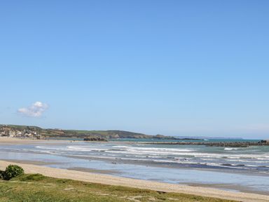 A beach with waves and a grassy area in the foreground and houses and hills in the background at The Baler House in Hayle