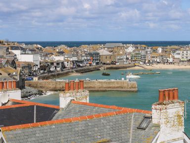 View of a coastal town with rooftops chimneys a harbor boats and the sea at The Baler House in Hayle