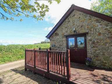 An exterior view of a stone building with double wooden doors and a wooden deck with railing at Bay View Barn in Hayle