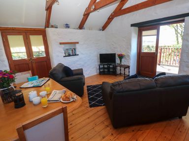 A living room with leather sofas a TV on a stand and a table with breakfast items at Bay View Barn in Hayle