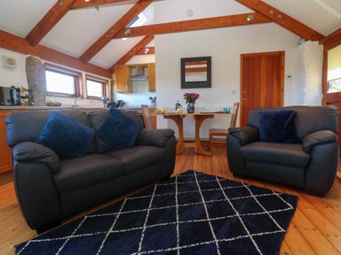 A living room with two sofas a dining table and chairs a kitchen area with wooden beams on the ceiling at Bay View Barn in Hayle
