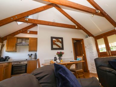 A kitchen and dining area with wooden beams on the ceiling and a table with flowers and croissants at Bay View Barn in Hayle