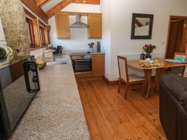 A kitchen with wooden cabinets a granite countertop a dining table with chairs and flowers at Bay View Barn in Hayle