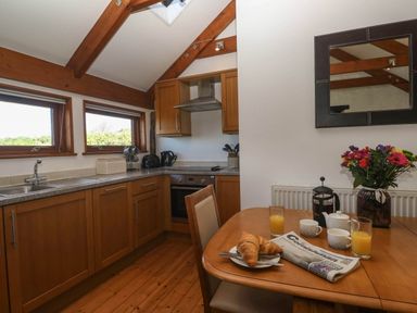 A kitchen with wooden cabinets a table set with croissants orange juice cups a coffee press and flowers at Bay View Barn in Hayle