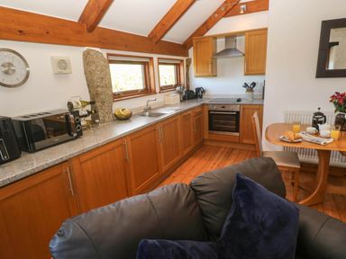 A kitchen with wooden cabinets countertop appliances a wooden dining table with breakfast and a black sofa with cushions at Bay View Barn in Hayle