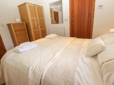 A bedroom with a double bed white bedding two wooden wardrobes a chest of drawers and a wooden door at Bay View Barn in Hayle