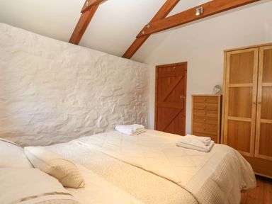 A bedroom with a bed, wooden wardrobe, chest of drawers and wooden door at Bay View Barn in Hayle