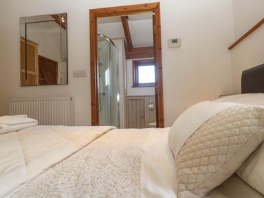 A bedroom with a bed and pillow facing a doorway leading to a bathroom with a shower at Bay View Barn in Hayle
