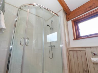 A bathroom shower enclosure with glass doors wooden paneling and a window at Bay View Barn in Hayle
