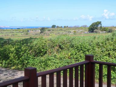 A view of green fields and bushes with a wooden railing in the foreground and a distant sea visible at Bay View Barn in Hayle
