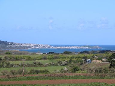 A coastal landscape view with fields and greenery in the foreground and a town by the sea in the background at Bay View Barn in Hayle