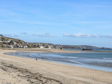 A sandy beach with a few people walking near the shoreline and a village in the background at Bay View Barn in Hayle