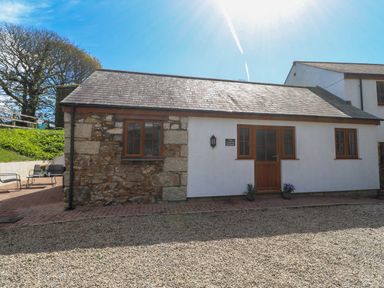 Exterior of a one-story building with stone and white walls and wooden framed windows at The Coach House in Hayle