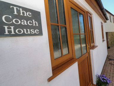 An exterior wall with a wooden door and window next to a sign that says The Coach House at The Coach House in Hayle