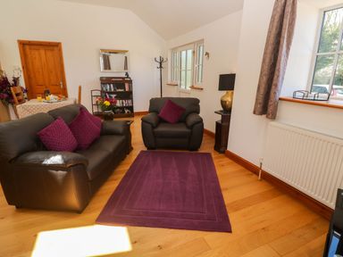 A living room with black leather sofa and armchair with purple cushions and rug at The Coach House in Hayle