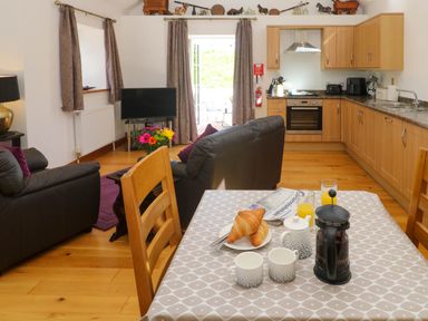 A kitchen and dining area with wooden cabinets and table set for breakfast with croissants and coffee at The Coach House in Hayle